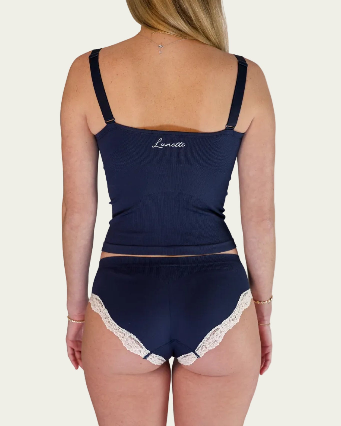 Back view of model wearing the Lunetti Luna Top and Luna Brief in Midnight Navy with white lace trim and logo embroidery across the back of the top.